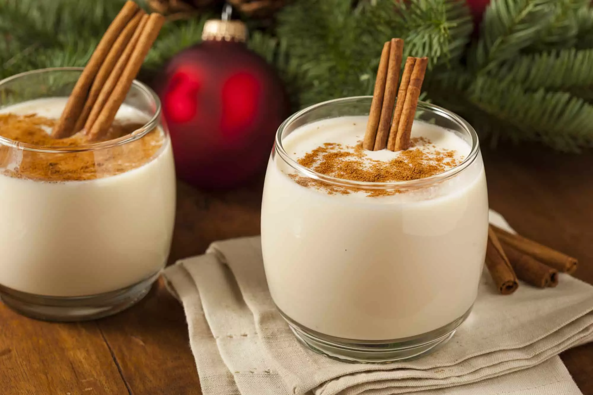 Two glasses of decadent, creamy non-alcoholic eggnog with cinnamon sticks and Christmas decorations