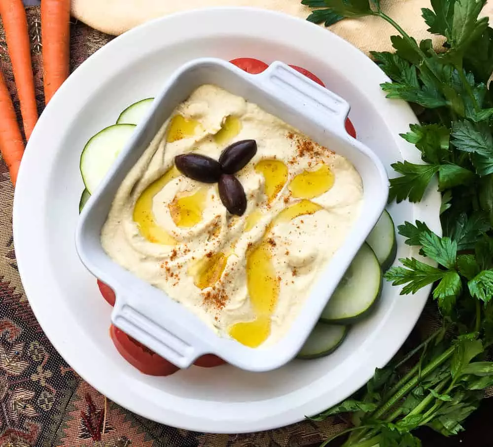 bowl of homemade roasted garlic hummus on a plate with vegetables