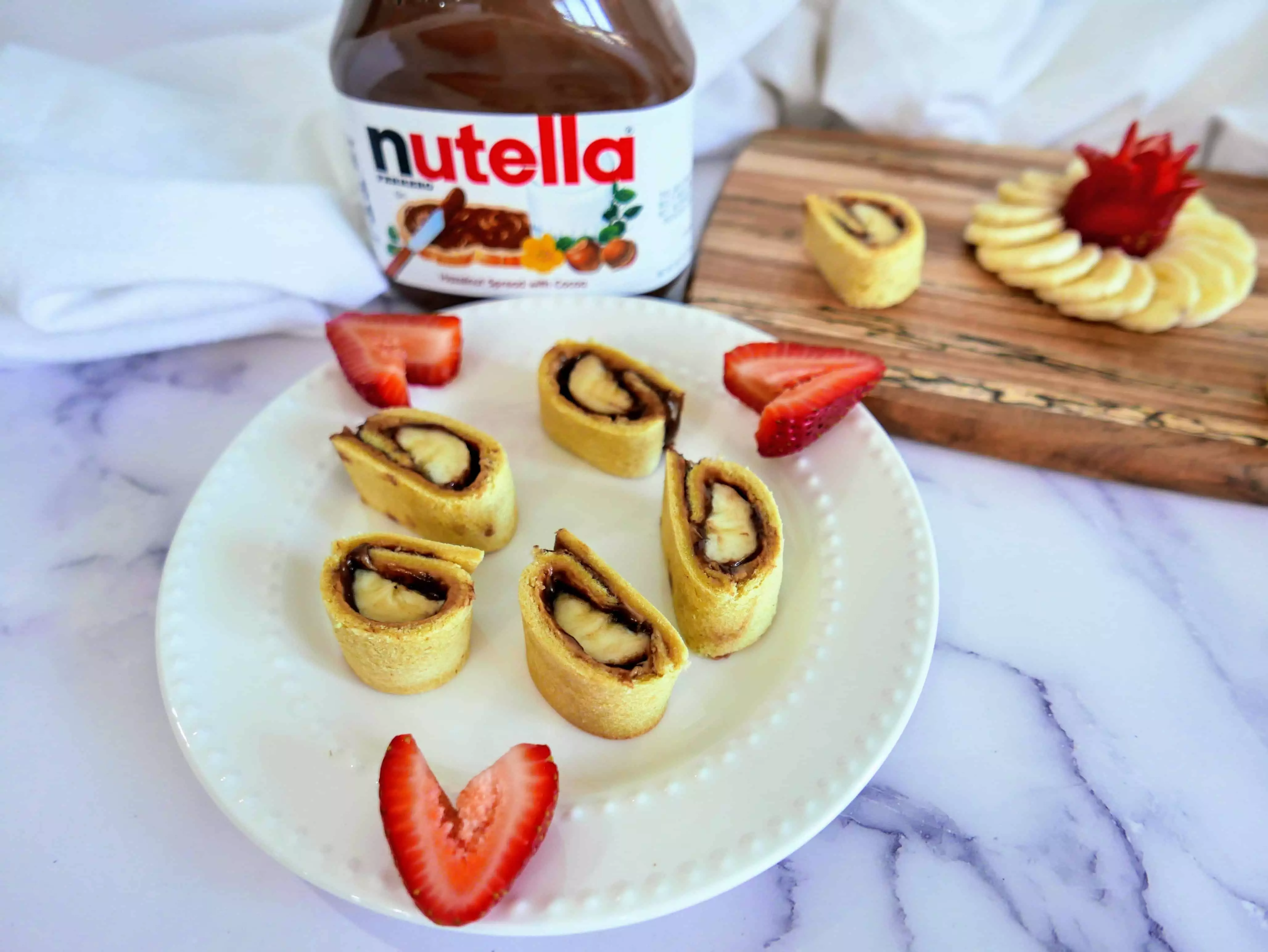 banana, peanut butter, Nutella sushi on a plate with cut up strawberries