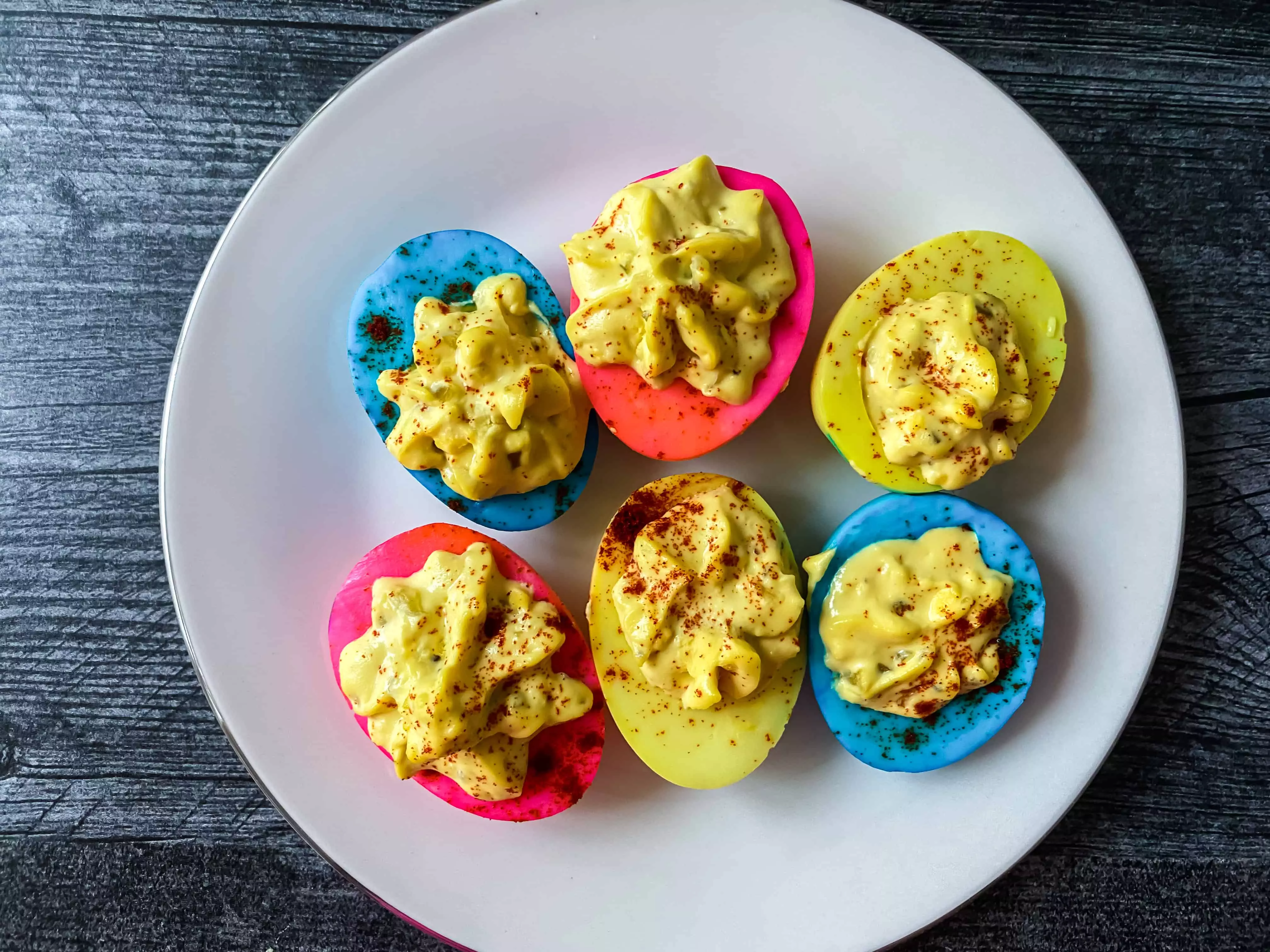 yellow, blue and pink colored deviled eggs on a plate