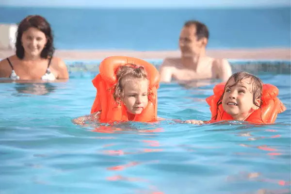 kids in pool wearing lifejackets with parents in background