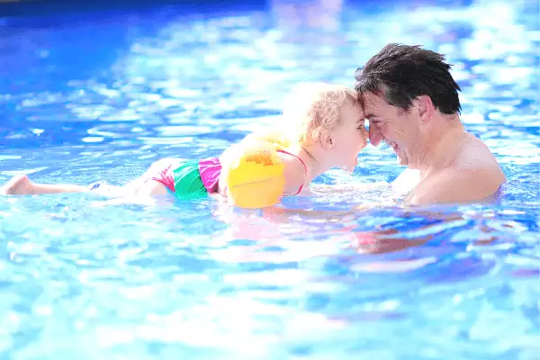 father holding his young daughter face to face in swimming pool