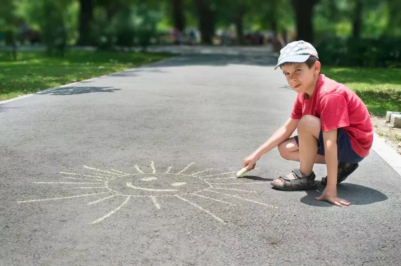 Little boy drawing a sun with chalk on the sidewalk