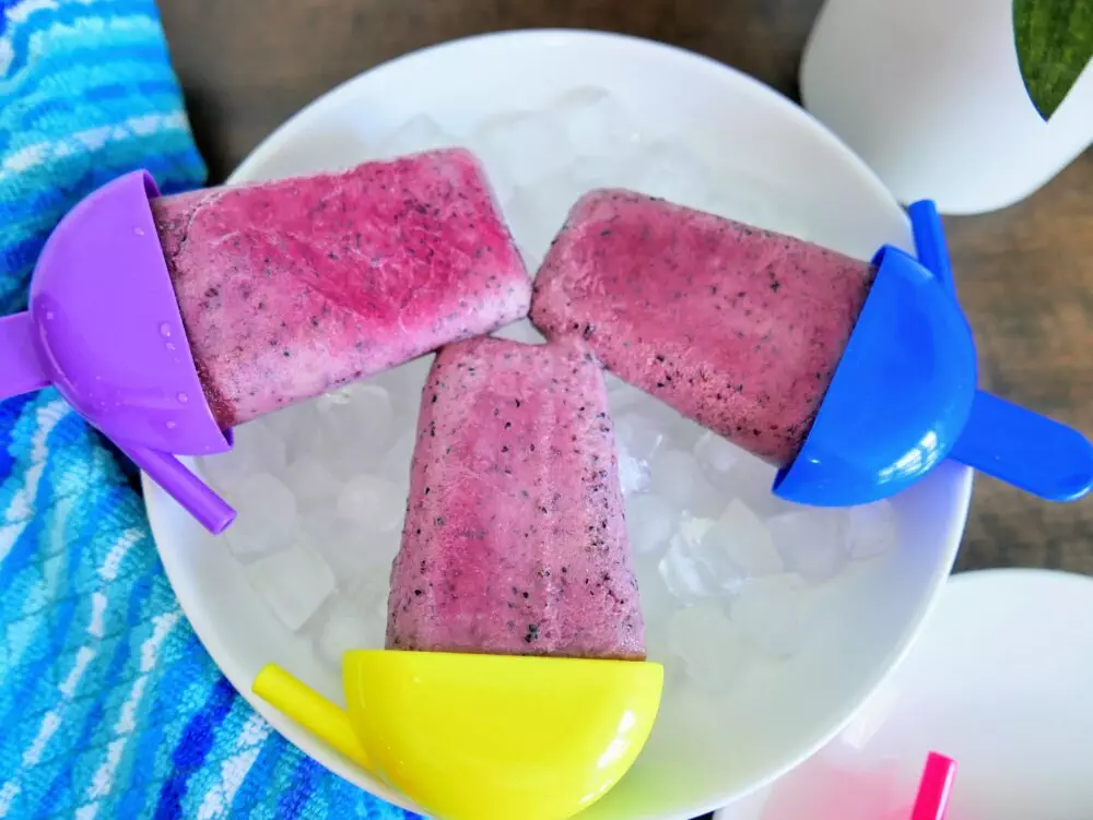 3 blueberry popsicles on a bowl of ice