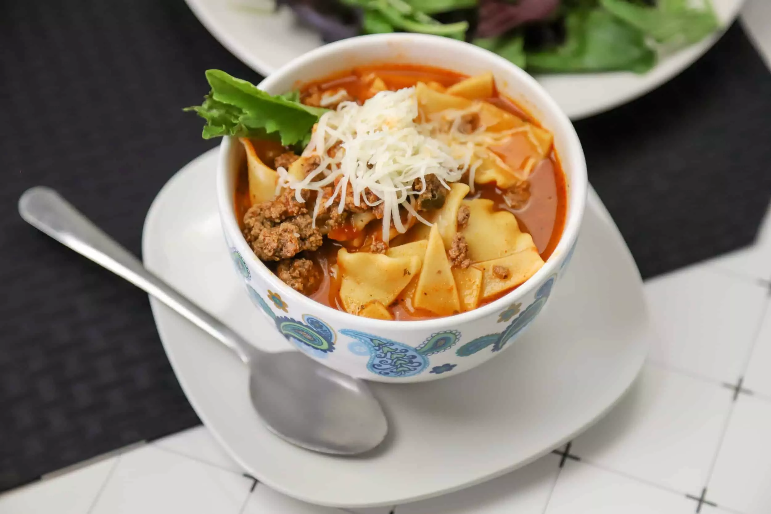 Instant pot lasagna soup in a bowl with a spoon and a side salad