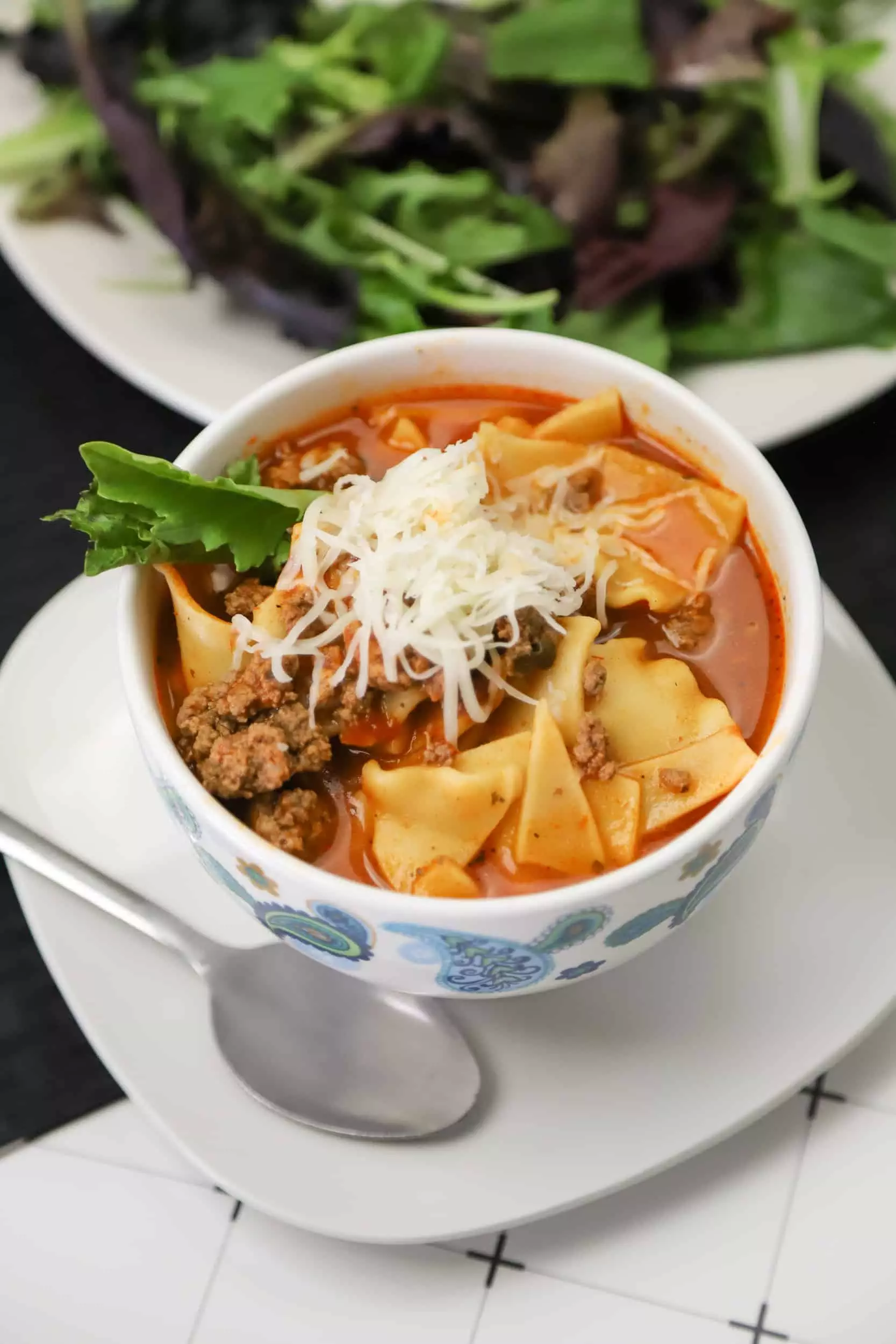 closeup of Instant pot lasagna soup in a bowl with a spoon and a side salad