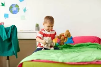 little boy playing with stuffed animals by his bed